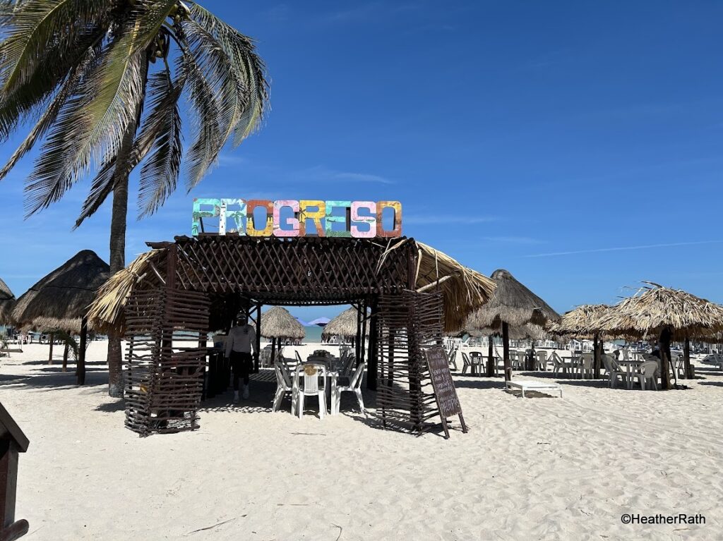 Smaller Progreso sign over a palapa on the beach